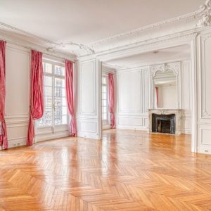 Ampia stanza di un palazzo d'epoca con parquet lucido, pareti e soffitti bianchi con stucchi e modanature