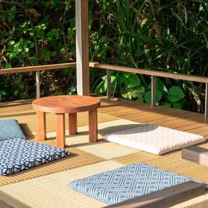 Area di un decking da esterno immerso nel verde, con stuoie, cuscini e sgabelli