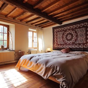 Camera da letto in abitazione rustica con travi a vista. Nella stanza ci sono due finestre,