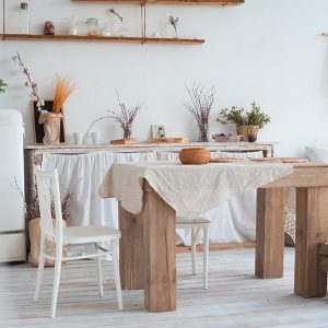 Luminoso open space con cucina, sala da pranzo e salotto in una casa di campagna. La stanza è tutta sui toni del bianco, al centro c'è un massiccio tavolo in legno e si vedono anche un frigorifero bianco, una