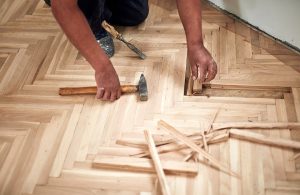 Un uomo di cui si vedono solo le braccia e le mani sta riparando alcuni elementi di un parquet usando un martello