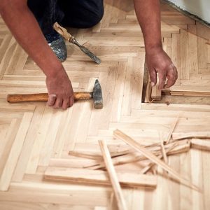 Un uomo di cui si vedono solo le braccia e le mani sta riparando alcuni elementi di un parquet usando un martello