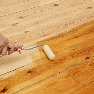 Mano di un uomo che con un rullo sta applicando dell'olio a un parquet