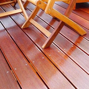 Dettaglio di un decking esterno in legno di bangkirai. Si intravedono anche le gambe un tavolo e sedie da giardino