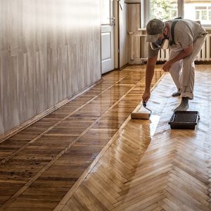 Un operaio sta oliando con un rullo un parquet a spina di pesce