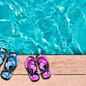 Vista dall'alto di due paia di infradito di colori diversi (azzurre e magenta) lasciate sulle assi in legno del decking a bordo piscina