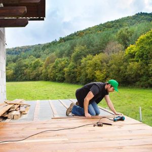 Un tecnico sta installando un parquet da esterno fuori da una casa immersa nel verde in una zona montuosa