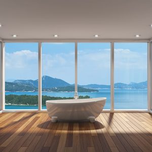 Stanza completamente finestrata con soffitto bianco e faretti, affacciata su un panorama costiero. Nella stanza, con pavimento in parquet, si trova soltanto una vasca da bagno bianca dalle linee moderne e tondeggianti