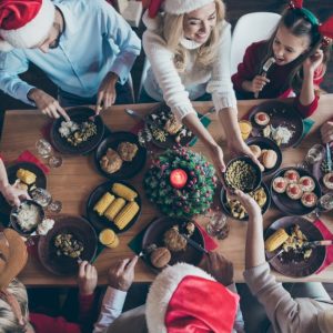 Vista dall'alto di una tavola imbandita per il Natale, con molte persone, grandi e bambini, che stanno pranzando con gioia indossando il cappello di Babbo Natale