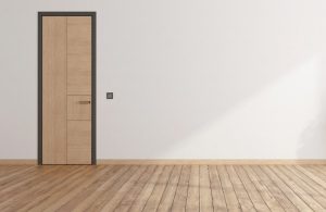 Una porta in legno alta e stretta con lo stesso colore di un parquet, in una stanza vuota con parete bianca