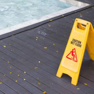 Un cartello giallo che indica il pericolo di pavimento scivoloso sul decking a bordo piscina