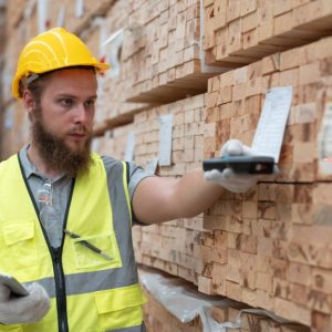 Un operaio di un magazzino di legname sta controllando i codici sulle assi di legno conservate in grandi scaffali