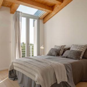 Camera da letto moderna in una stanza con parquet, soffitto con travi a vista, finestre e velux