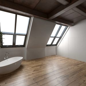 Sottotetto mansardato con finestre, travi a vista e soffitto a cassettoni in legno scuro, parquet medio-chiaro e vasca da bagno minimale bianca