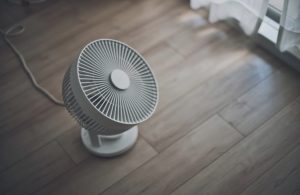 Un ventilatore poggiato su un pavimento in parquet, visto dall'alto