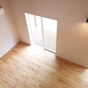 Vista dall'alto di uno spazio interno vuoto, con pareti bianche, pavimento in parquet e porte a vetri scorrevoli da cui entra luce naturale